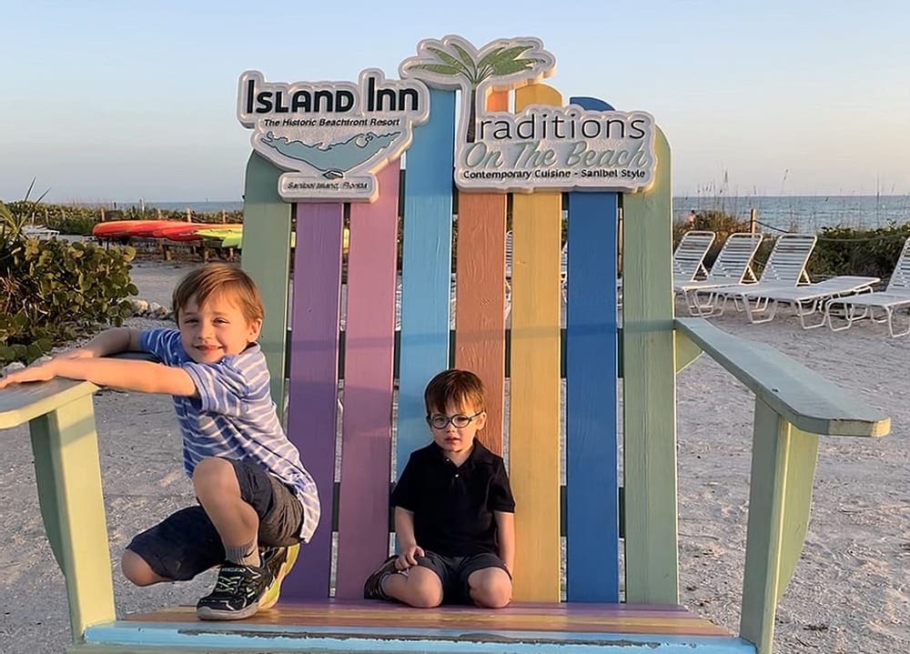 Two brothers sit on a colorful, oversized Adirondack chair on the beach at Sanibel Island.
