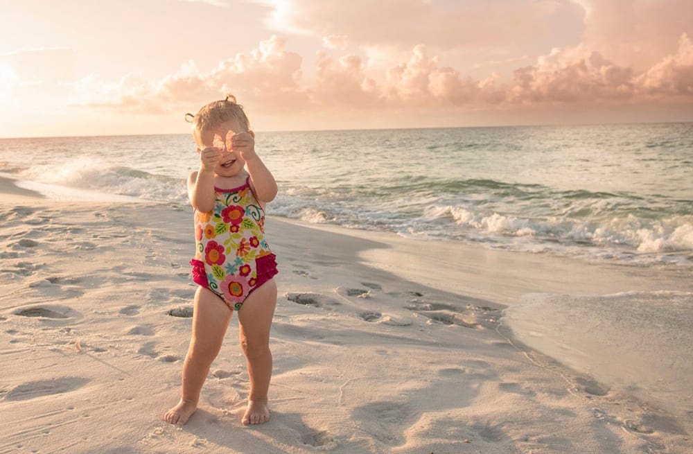 Toddler girl in red floral bathing suit playing on sand at Navarre Beach in Florida
