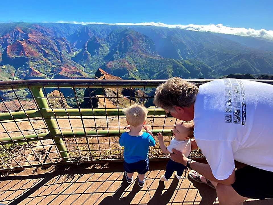 Man stands with two young kids looking out over a Hawaiin landscape in Kauai.