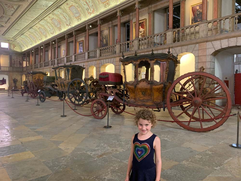 Little girl in front of coach in National Museum in Lisbon.