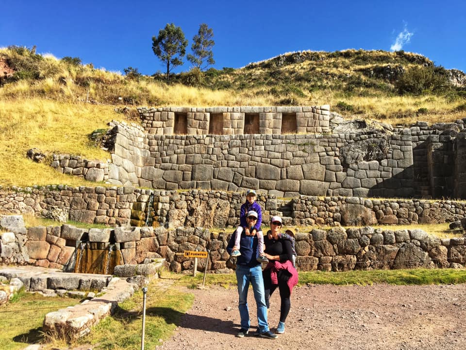 Family of three stands in front of an ancident ruin within the Sacred Valley of Peru.