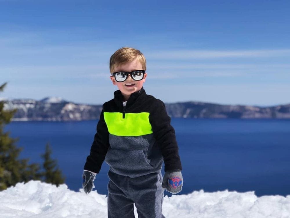 Boy stands smiling in the snow at Crater Lake National Park