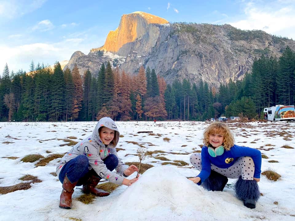 Two young girls crouch in the snow while building a snow hill at Yosemite National Park.