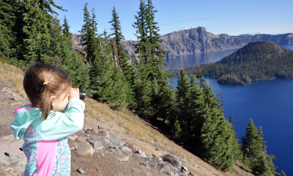 A young girl looks across Crater Lake through binnoculars.