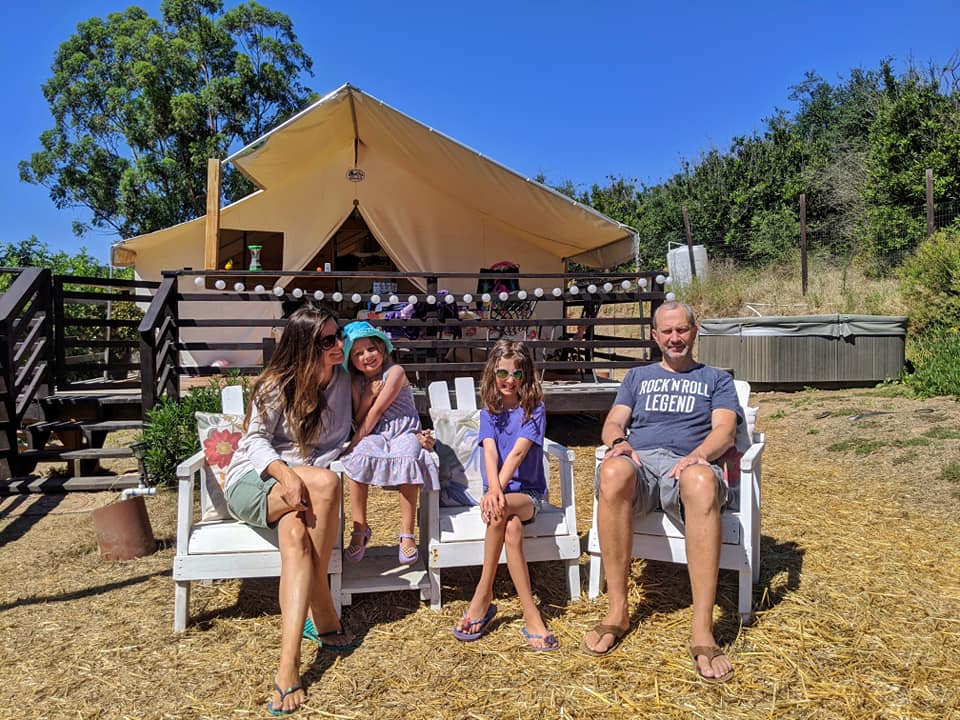 A family of four sits smiling in front of a luxury tent.