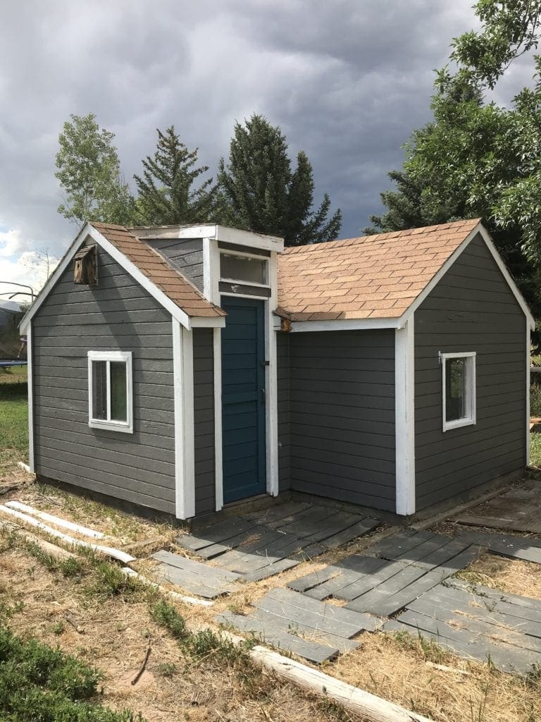 View of a small outdoor playhouse with dark gray paint and white trim.