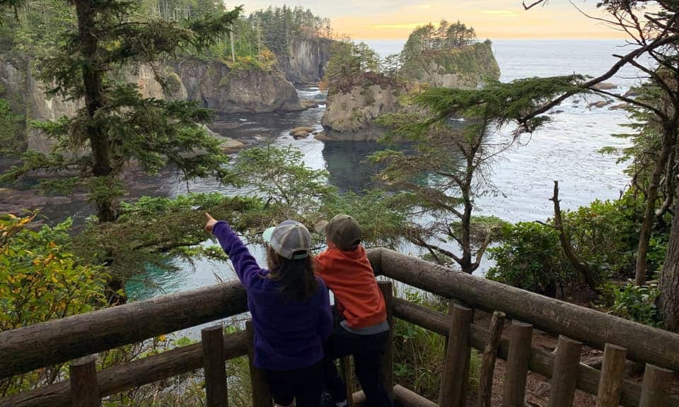 Two kids look over and outlook onto cliffs and water near Olympic National Park, one of the best Summer Vacation Ideas in the U.S. for Families.