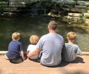 Dad with 2 little kids sitting on the side of the river