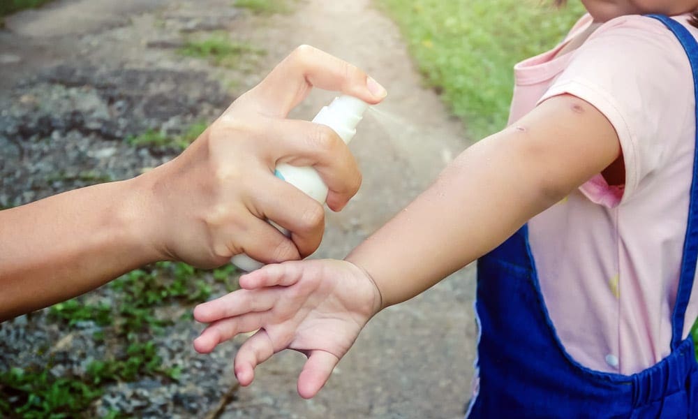 An adult hand with a bug spray bottle sprays the arm of a child. Insect repellent is key for any travel first aid kit for kids.