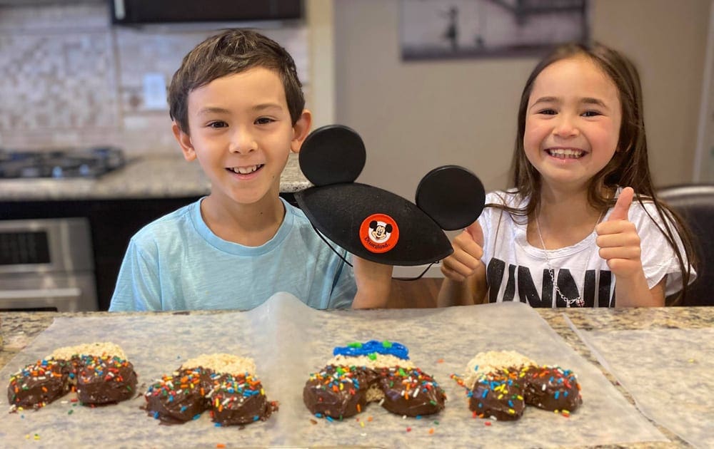 Two kids pose with a Mickey Mouse hat and Mickey Mouse shaped rice cereal treats.