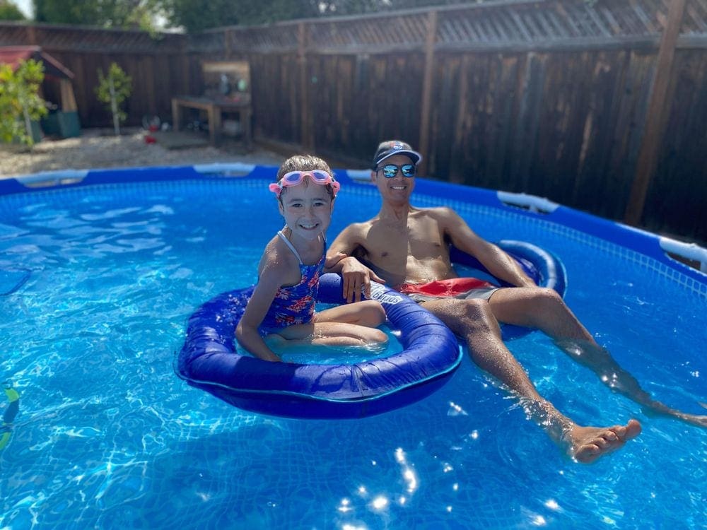 Father and daughter float in a pool in the backyard.