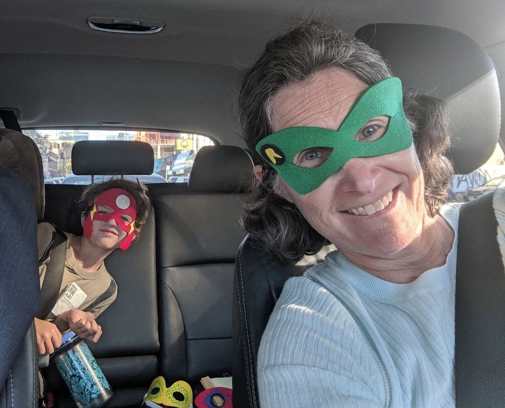 Mother and son wear super hero masks while in the car. Inventing silly stories involving super heros or other topics is a great family road trip game.