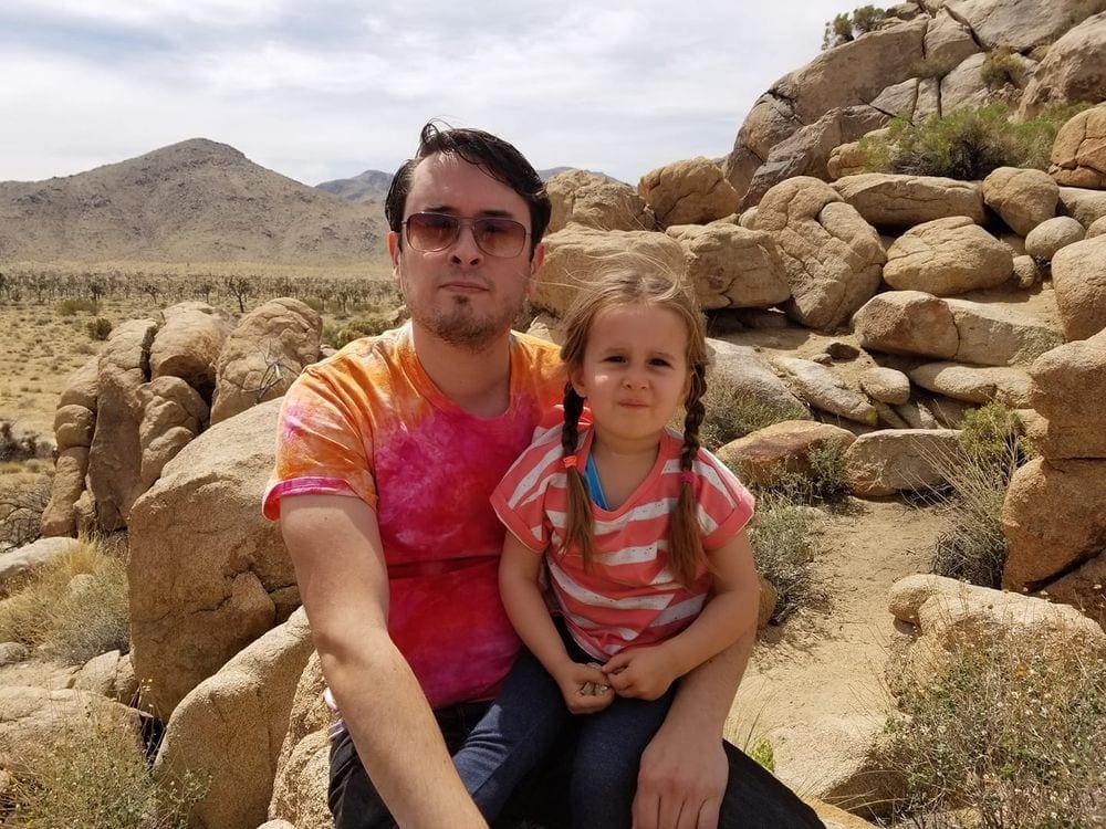 Father and daughter sit among dessert rocks within Joshua Tree National Park.