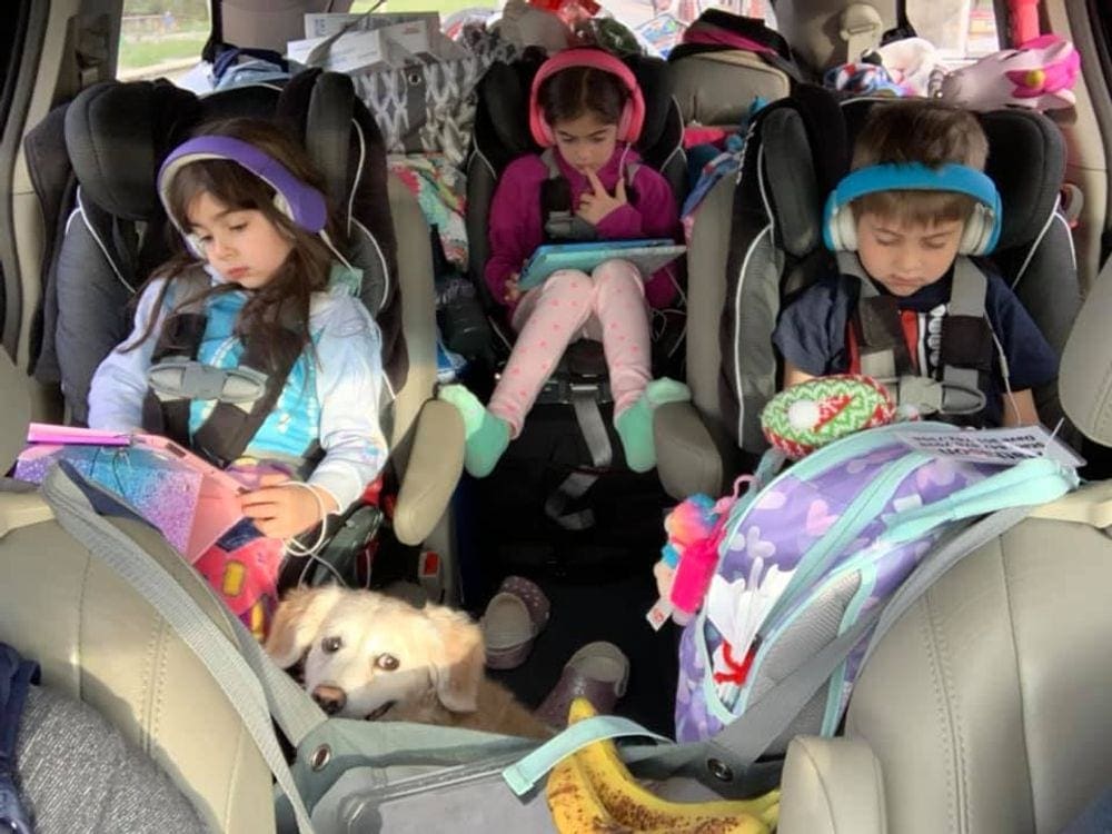 Three young kids sit in the back seats all wearing headphones using their own tablets. Listening games are some of the best family road trip games.