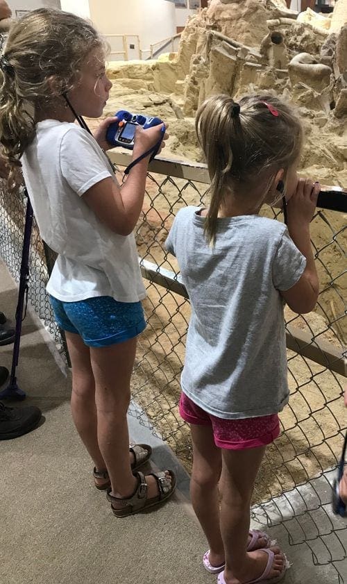 Two young girls stand at the edge of an exhibit at Mammoth Site, peering in to see the fossils.