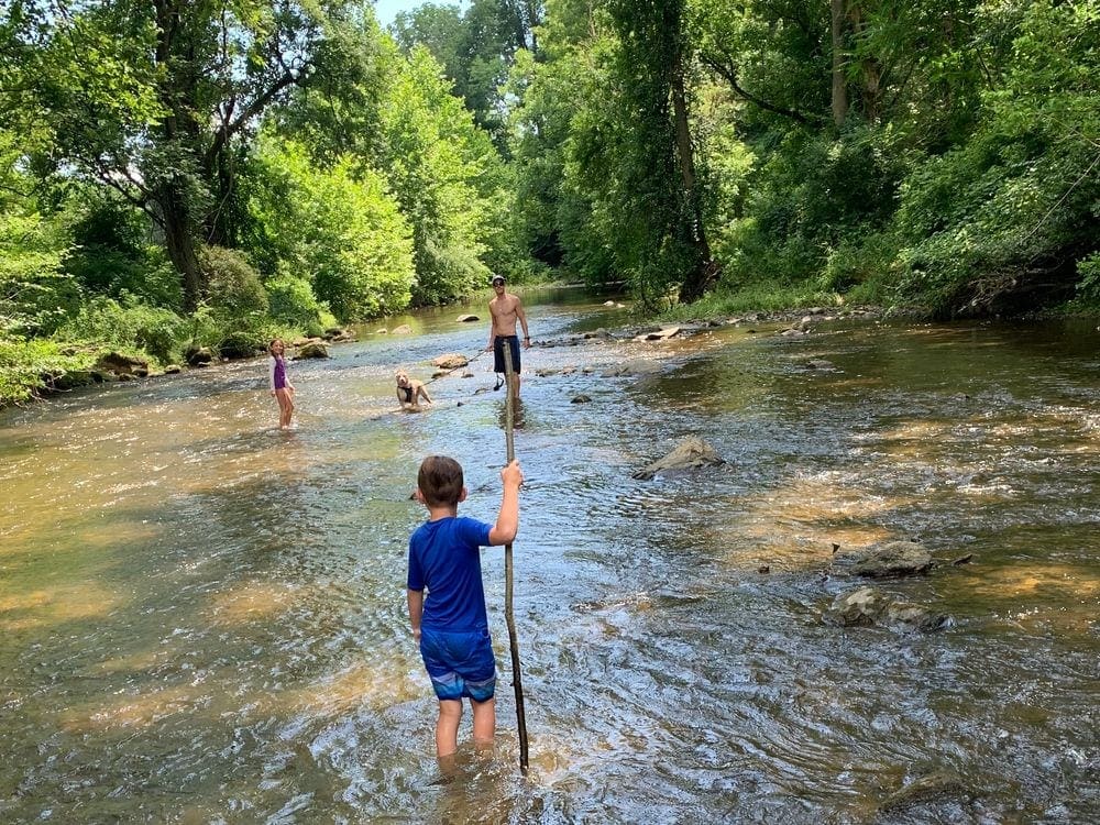 Dad stands in a large river with his two kids and dog. Exploring the great outdoors is one of our top 8 family staycation ideas.
