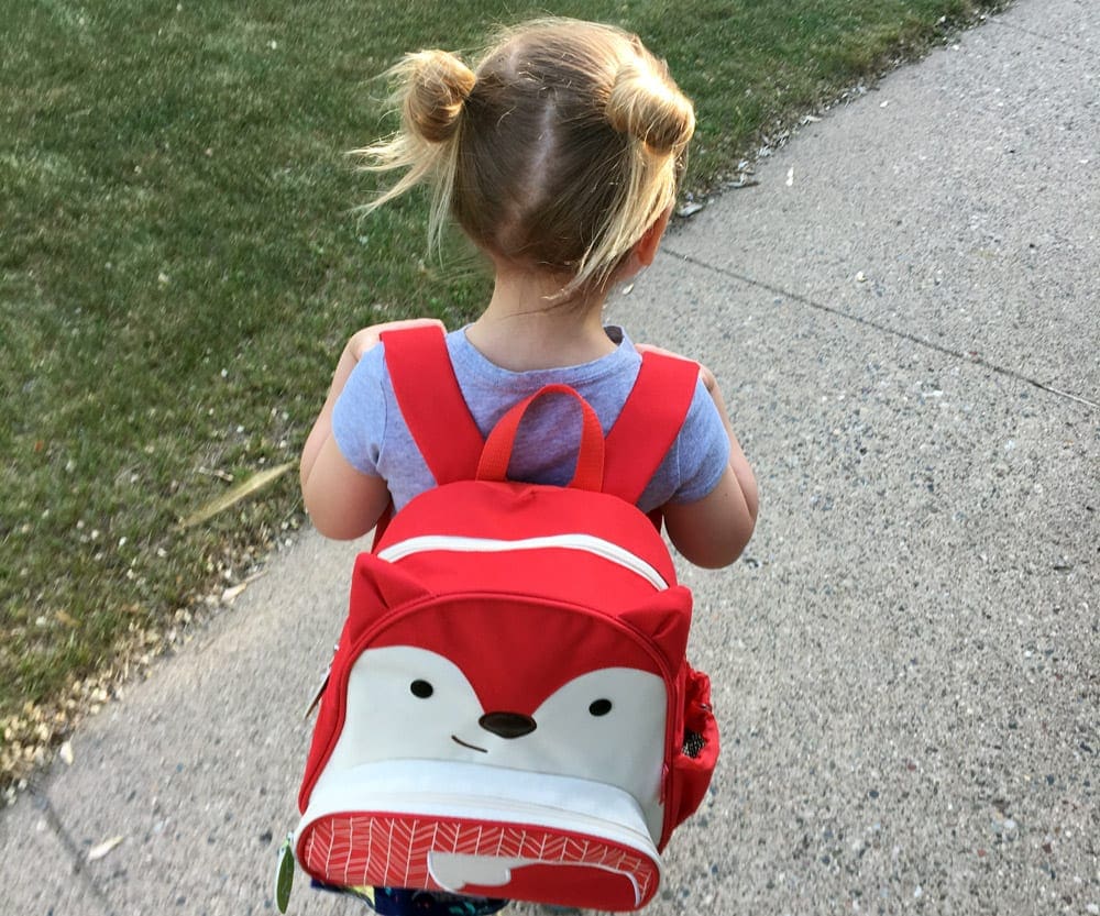 Small girl wearing a fox backpack.