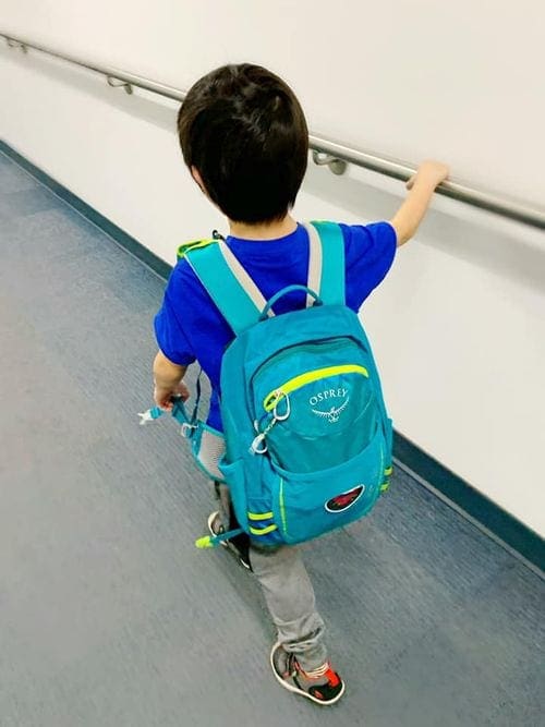 Small boy walks with blue backpack in the airport.