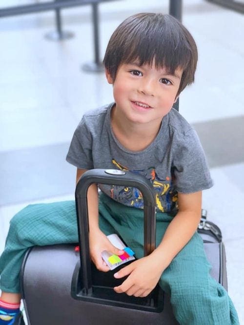 Small boy sits on a suitcase in an airport.