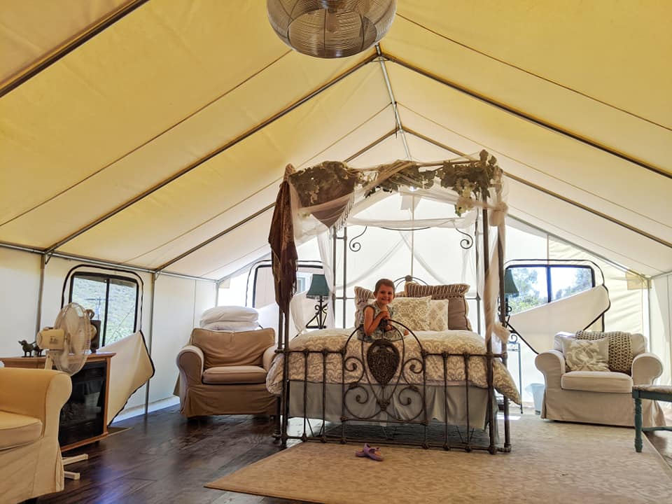 A little girl sits on a bed inside a large luxury tent, Your Guide To Family Glamping in Style