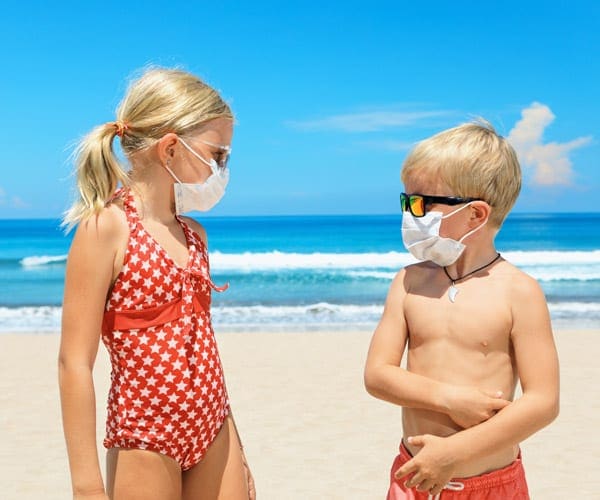 Two kids on the beach wearing a mask and looking at each other