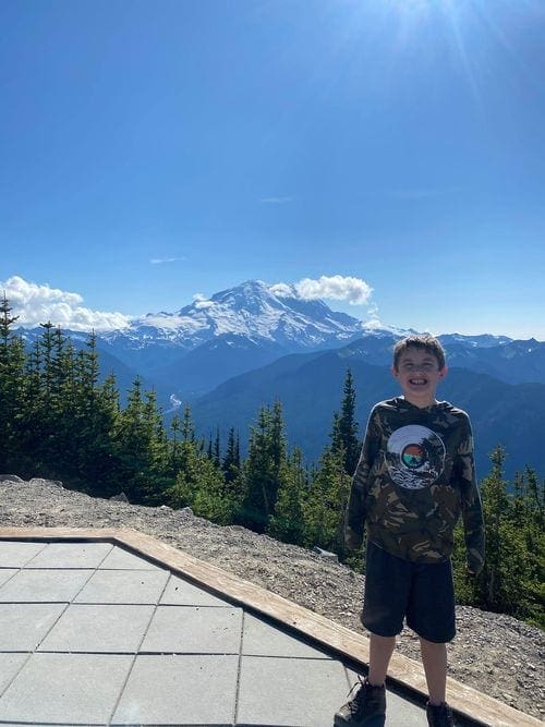 A 4th grade boy stands proudly view a view of Mt. Rainier in the background.