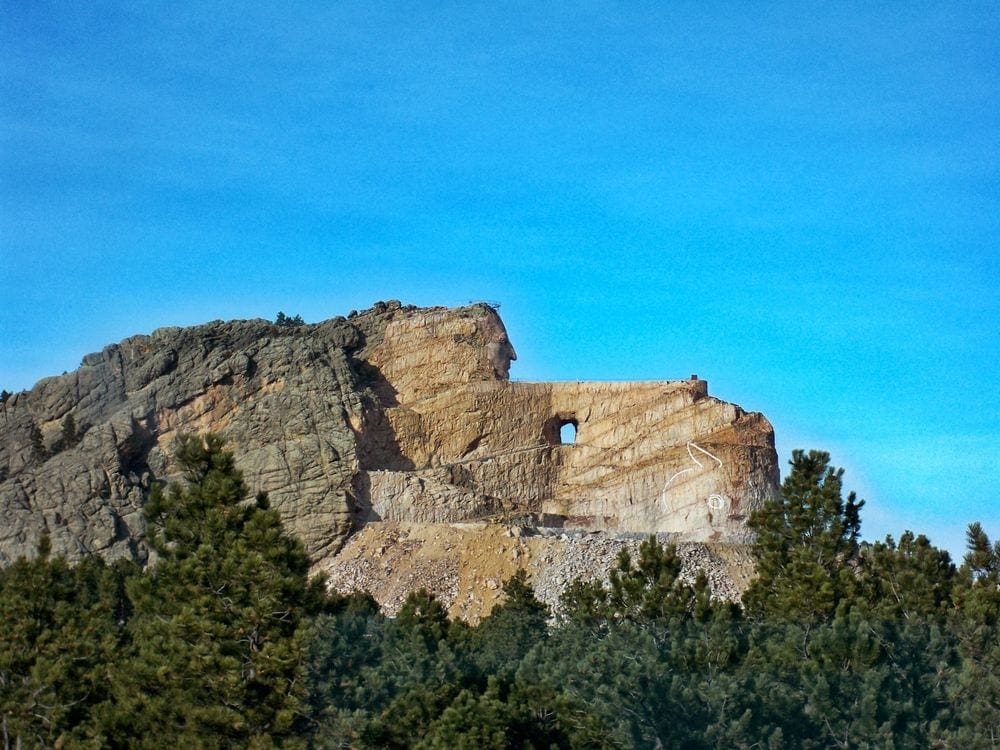 A view of the Crazy Horse Memorial, peaking over the treeline. When on a a Black Hills vacation with kids, Crazy Horse Memorial is a must see.