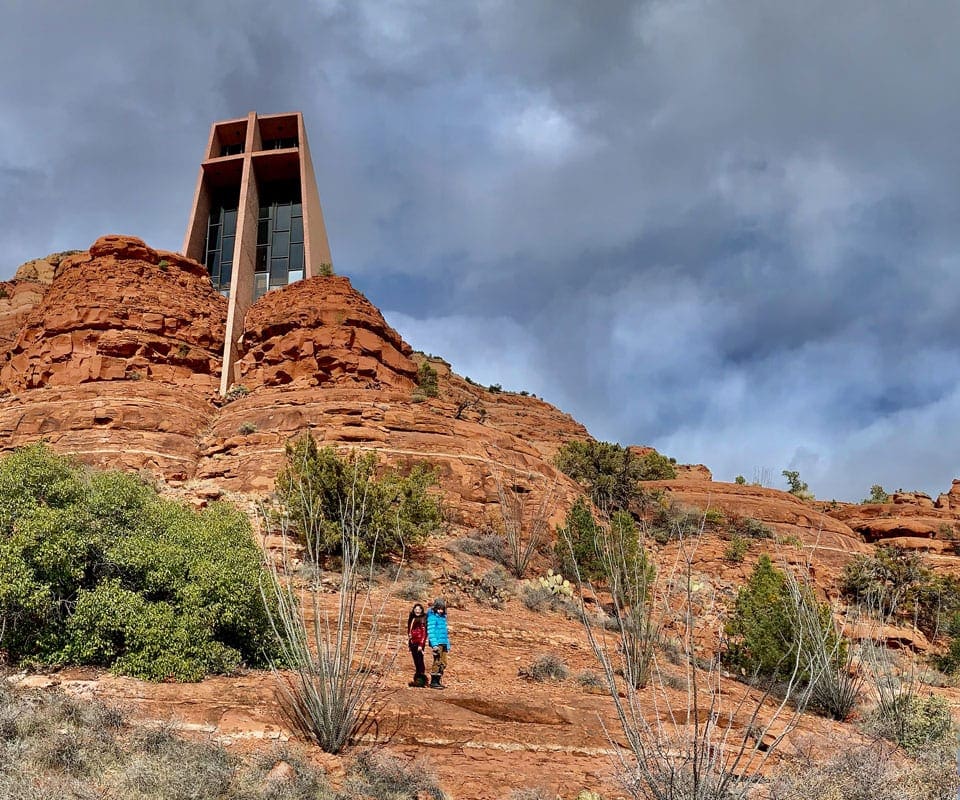 Two people posing back to back under The Chapel Of The Holy Cross, one of the best things to do in Sedona for families. 