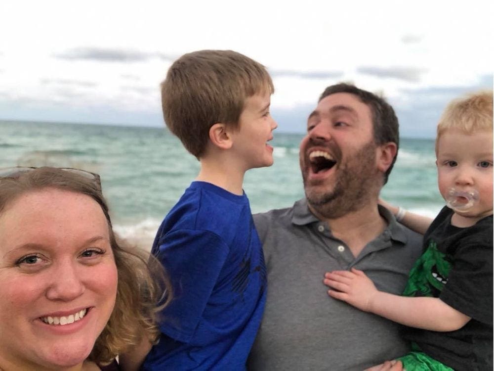 A family of four beams while they take a selfie in front of an ocean-scape. Experiencing the joy of your children is one of the best benefits of traveling with kids.