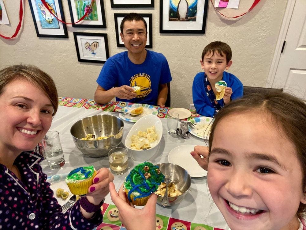 A family of four sits smiling around a dinner table enjoying cupcakes and other special treats. A family dinner party is a great way to recharge your batteries as a family.