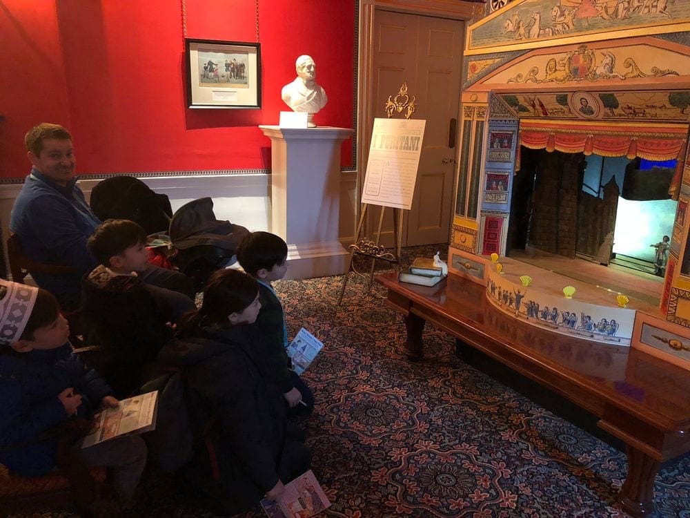A father and his four children look on at a puppet show scene inside the Kensington Palace.