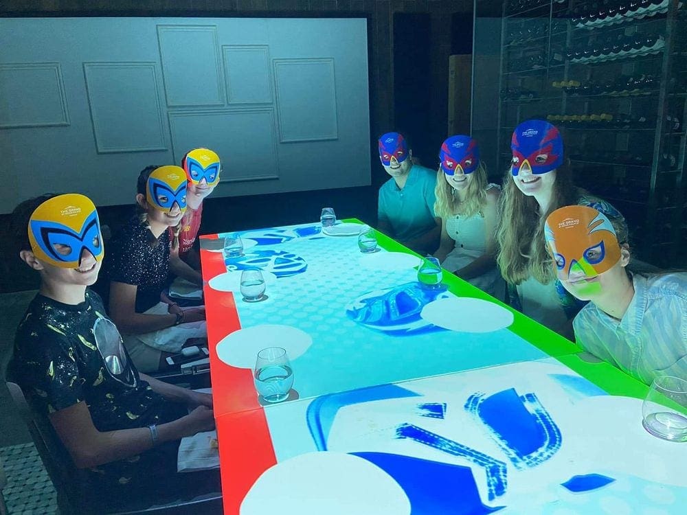 Seven kids and teens sit at a table prepared for a fun super-hero themed dinner at the Grand at Moon Palace Hotel, one of the best family resorts Cancun.