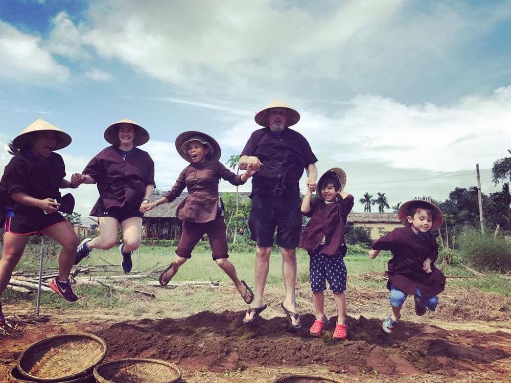 Six people with traditional Vietnamese hats on jump with huge smiles on their face. Developing respect for diverse cultures and identities is one of the most critical benefits of traveling with kids.