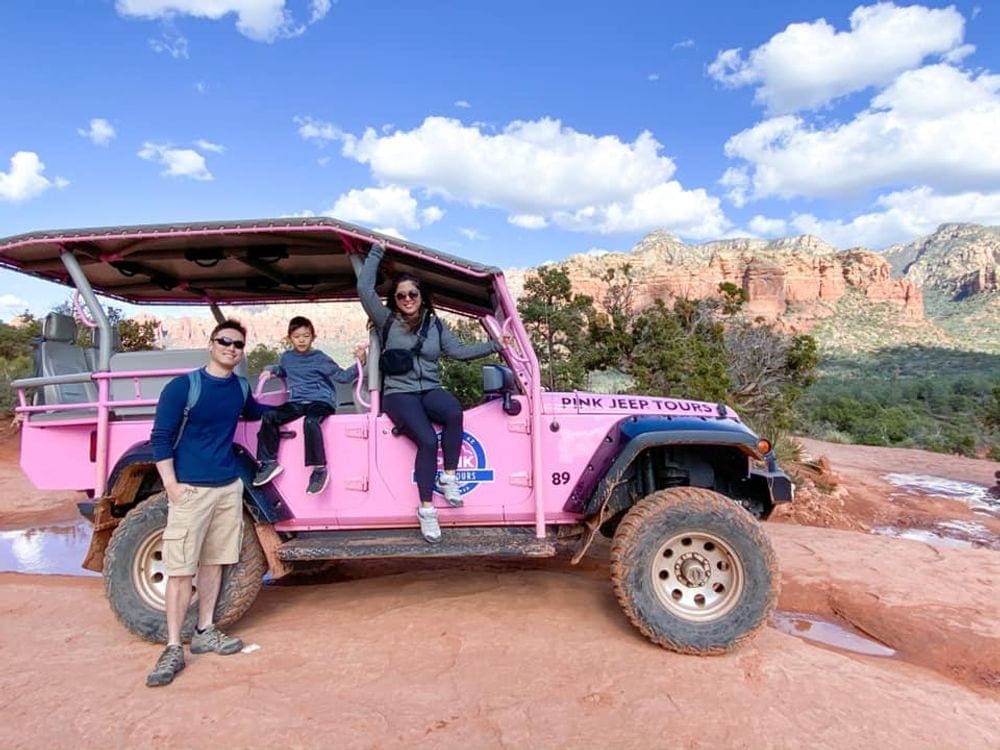 Two parents with their young child sit on a pink jeep as part of their Pink Jeep Tour in Sedona, truly one of the best things to do in Sedona for families.