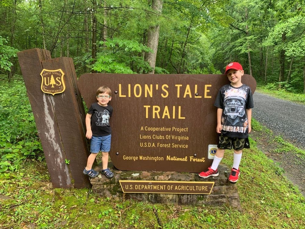 Two boys flank the entrance sign for Lion's Tale Trail, part of George Washington National Forrest in Virginia. Outdoor activities are great options for travel with kids during. COVID-19.