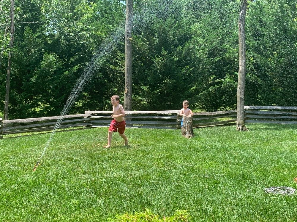 Two boys run through a large spray of water coming from a sprinkler. Finding kid-friendly, yet safe activities is critical to fun travel with kids during. COVID-19.