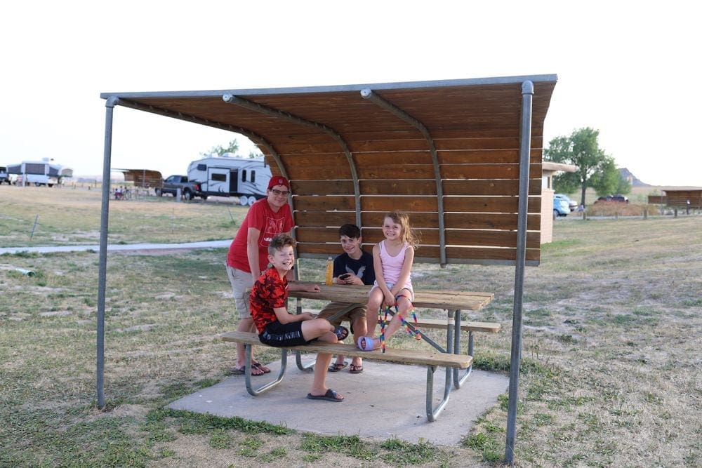 A dad and three kids sit under a sheltered picnic table, all smiling at the camera.