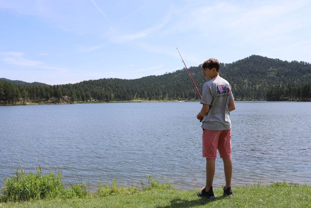 A young boy holds a fishing pole at the edge of a large lake.