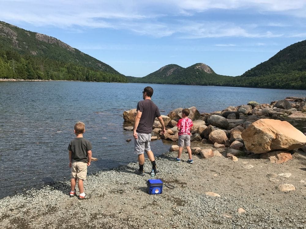 A father and his two sons throw rocks into the water at Acadia National Park.