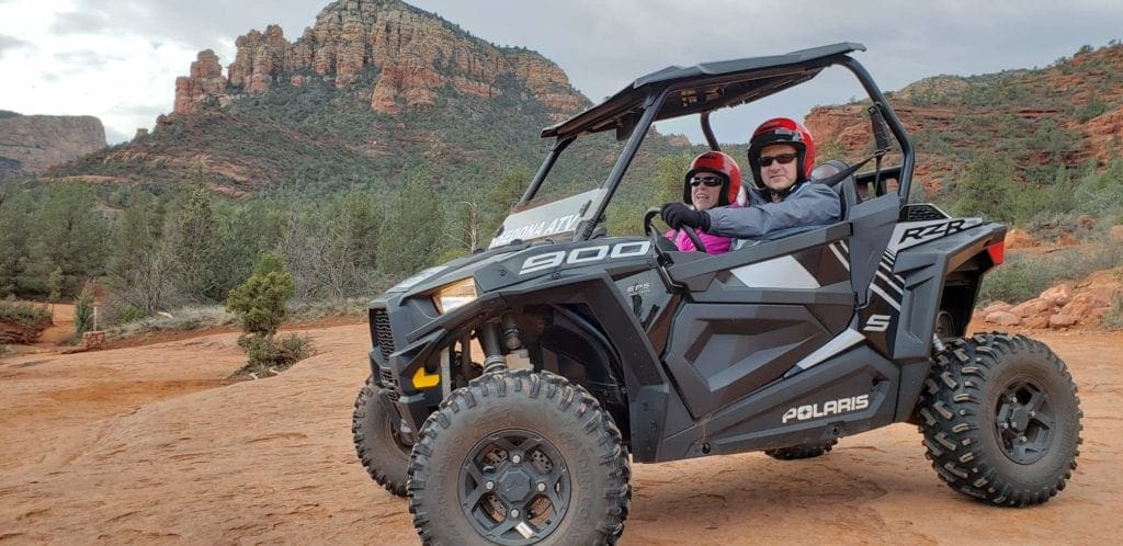 Two adults sit in an ATV exploring the Sedona desert.