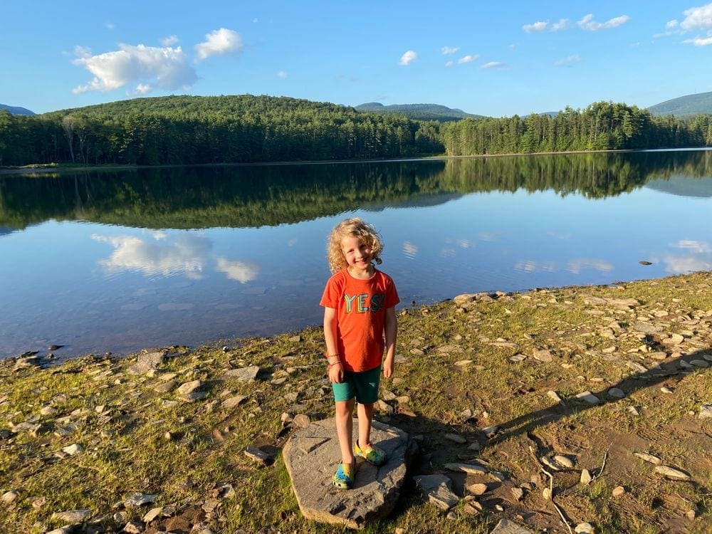 A young boy stands in front of a crystal clear lake in the Catskill Mountains.