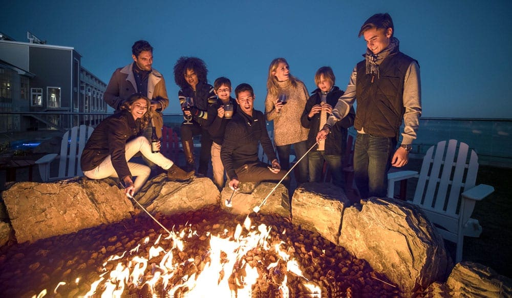 A large group of guests roasts marshmallows in an on-site fire pit at Cliff House, one of the best Maine hotels for families.