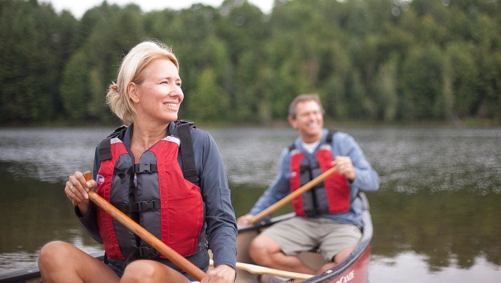 An adult woman and man canoe within the grounds of the Topnotch Resort, one of the best Vermont hotels for families.