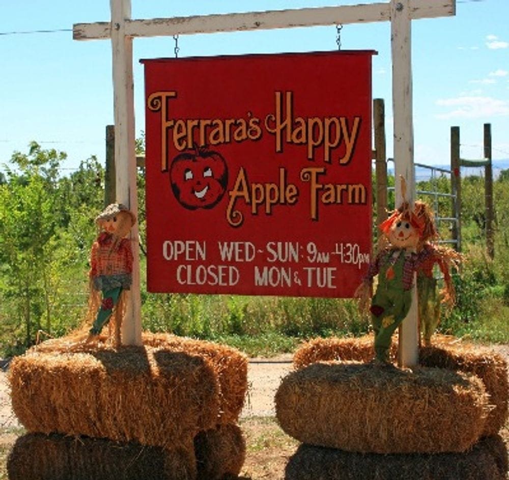 The entrance sign for Happy Apple Farm is flanked by hay bales and scarecrows.