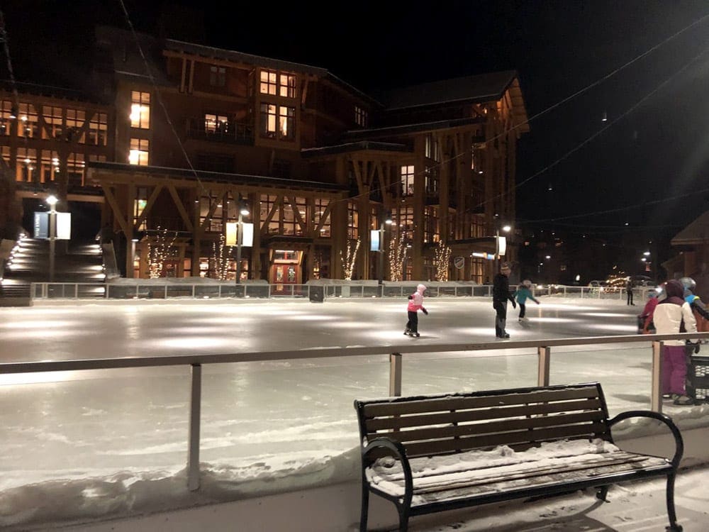 A few ice skaters enjoy an evening skate on the ice rink at Spruce Peak, one of the best Vermont hotels for families.