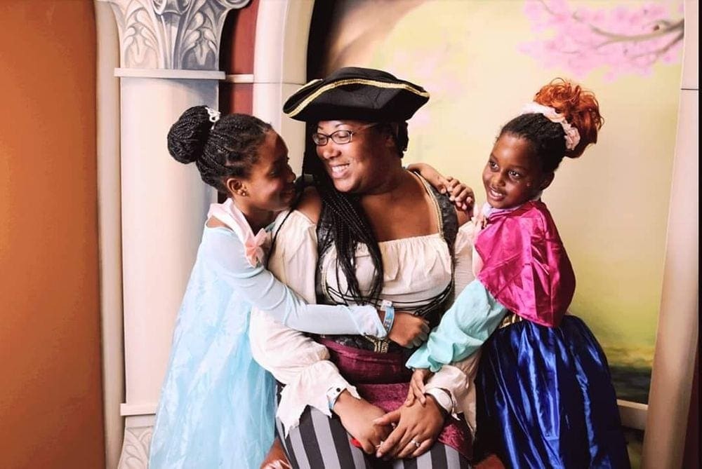 A black mother dressed as a pirated sits smiling at her two daughters, one dressed as Elsa, the other as Anna at Walt Disney World in Orlando, one of the best Thanksgiving destinations in the United States for families.