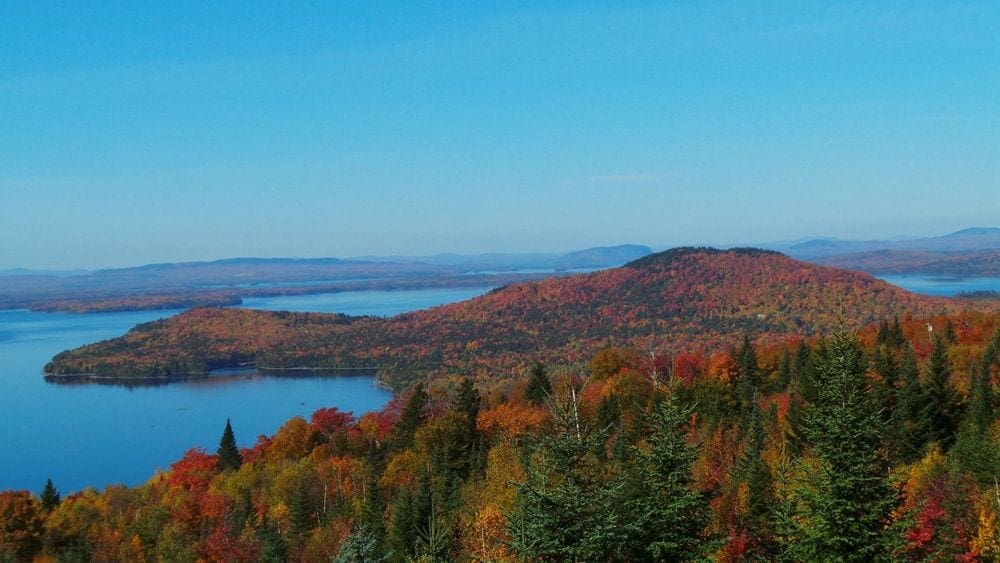 A semi-ariel view of Moosehead Lake with sweeping fall foliage, including hues of green, red, and yellow.