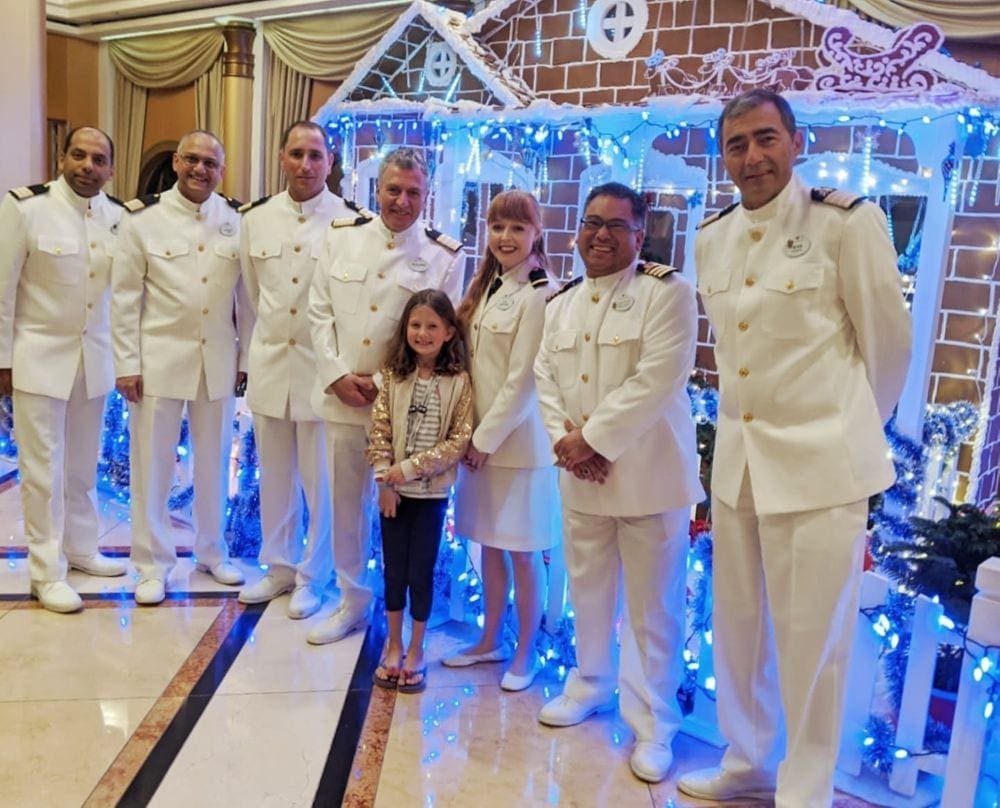 A young firl stands with seven crew members, including the captain on a Disney cruise.