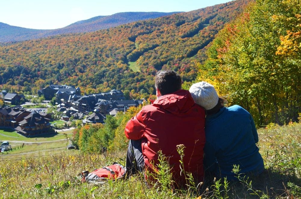 Two adults cuddle while looking over an expansive view of fall foliage at Spruce Peak, one of the best Vermont hotels for families.