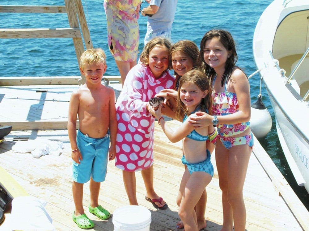 Five small kids huddle around one of the children holding a fish on a dock at Spruce Point Inn Resort & Spa in Maine, one of the best Maine hotels for families.